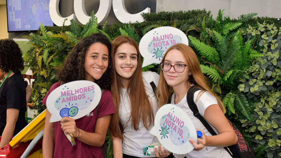 Três estudantes segurando placas e sorrindo.